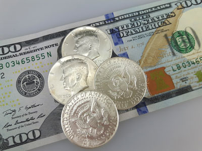 stock image: Kennedy silver coins laying on 100 dollar bill