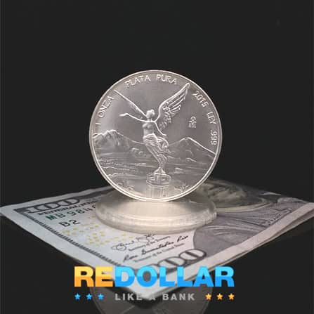 A 1 troy ounce Mexican Silver Libertad placed on a 100 dollar bill.